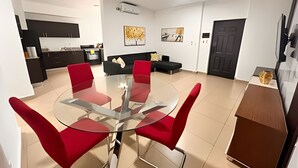 A modern living room with a glass-top dining table surrounded by red chairs, a black sofa, and a dark door. - Apartment in San Francisco (Panama City)