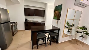Una cocina moderna con armarios oscuros, un refrigerador de acero inoxidable y una mesa de comedor con dos sillas.