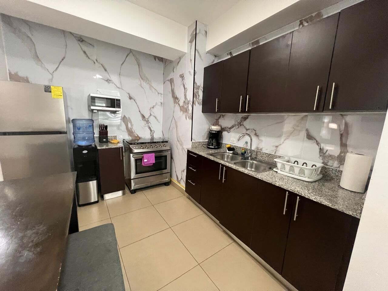 Una cocina compacta con armarios oscuros, un refrigerador de acero inoxidable, un microondas, una estufa y un lavamanos.