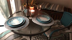 Een ronde glazen tafel met twee borden, een kaars en twee wijnglazen.