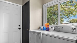 A laundry room with a white door, a washing machine, and a window with a view of trees.