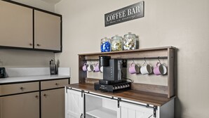 A kitchen with a coffee bar, including a coffee machine, jars, and cups.
