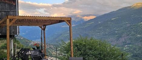 Une pergola en bois avec un espace salon extérieur, offrant une vue sur un paysage montagneux.