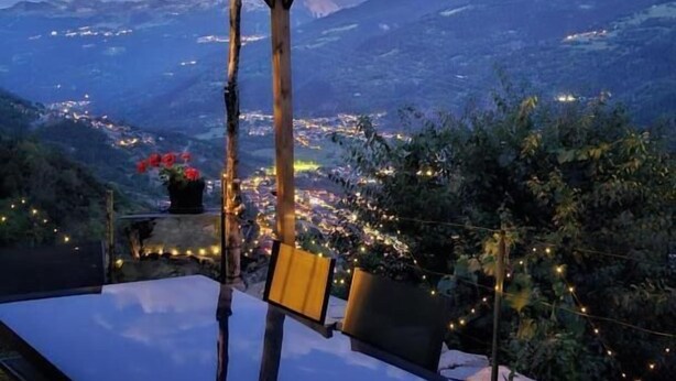 Una mesa con sillas bajo una pérgola, con vistas a un pueblo y montañas.
