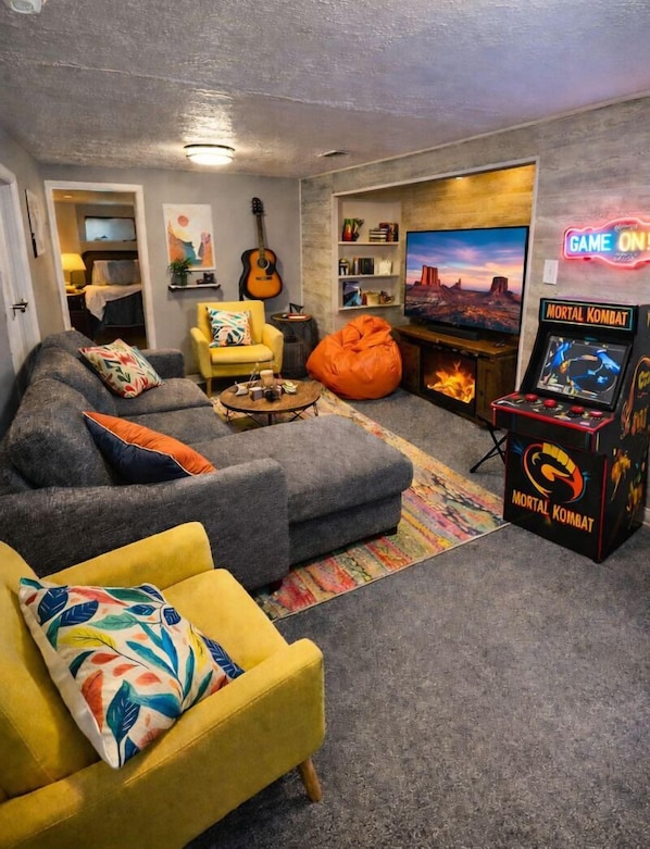 Ein Wohnzimmer mit grauem Sofa, gelbem Sessel und einer Spielkonsole.