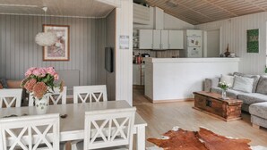 Eine moderne Küche mit weißen Schränken, ein Essbereich mit weißen Stühlen und ein Wohnzimmer mit einem grauen Sofa.