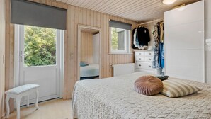 Ein Schlafzimmer mit Bett, Schminktisch, Bank und einem Fenster mit Blick auf Grünflächen.