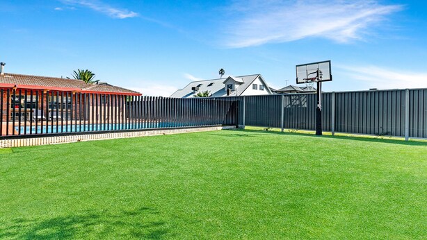 Un jardin avec une piscine, un panier de basket et une zone délimitée par une clôture.