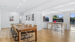 Une pièce spacieuse avec une longue table et des chaises en bois, un coin cuisine avec une fenêtre, et une vue sur une piscine.