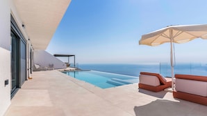 Un espace piscine extérieur moderne offrant une vue dégagée sur l’océan, avec un fauteuil de relaxation et un parasol.