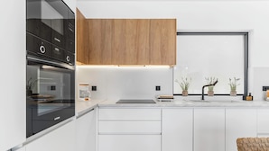 Une cuisine moderne avec des meubles blancs, un four noir et des placards supérieurs en bois.