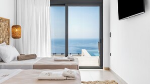 Une chambre d’hôtel avec deux lits, une grande fenêtre donnant sur la mer, un téléviseur fixé au mur et un luminaire en fibres tressées.