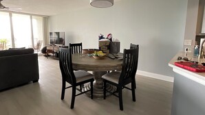 A dining area with a round table, four chairs, a television, and a ceiling fan.