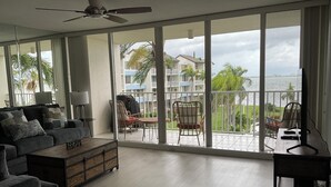 A spacious balcony with a view of the sea and buildings, furnished with a sofa, chairs, and a table.