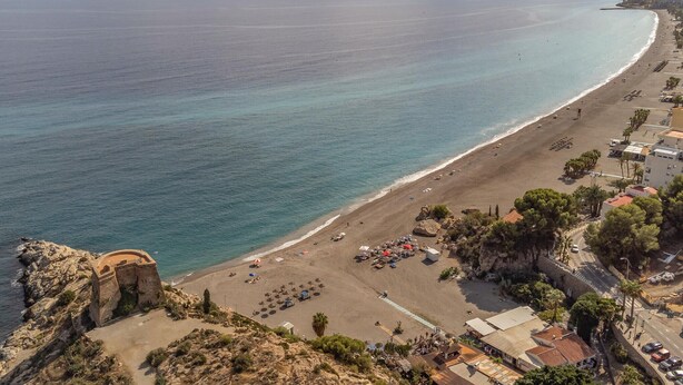 A coastal beach with a rocky cliff, a clear view of the sea, and a row of buildings along the shore. - 2 bedroom cozy apartment in Almunecar (Almunecar)