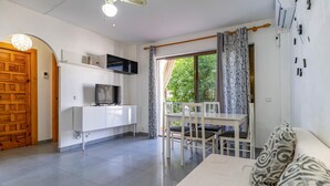 A modern living room with a TV, white furniture, and a balcony with curtains. - 2 bedroom cozy apartment in Almunecar (Almunecar)