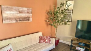 Un salon avec un canapé beige, une plante en pot rouge, un téléviseur à écran plat et une table basse en bois.
