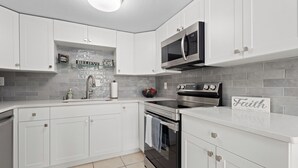 Una cocina moderna con armarios blancos, un microondas de acero inoxidable y salpicadero de azulejos.