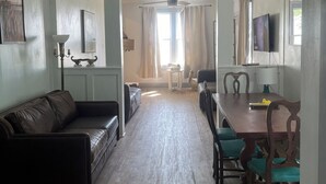 Amplia sala de estar con ventilador de techo, comedor con mesa y sillas, y un gran ventanal que permite la entrada de luz natural.