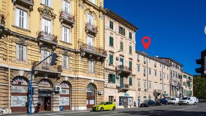 A row of historic buildings with traditional balconies and shutters, a yellow car parked on the street, and a pedestrian crossing.