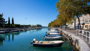 A calm waterfront with boats docked along the pier, a clear sky, and buildings on the right.