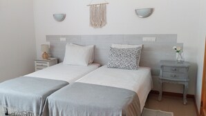 Ein Doppelbett mit zwei Kissen, ein Nachttisch mit Lampe sowie eine wandhängende Makramee-Dekoration.