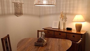Ein Essbereich mit einem runden Holztisch, Stühlen, einer hängenden Leuchte, einer Wanddekoration aus Makramee und einer Lampe auf einer Holzkommode.
