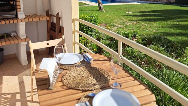 Eine Holzterrasse mit Tisch für zwei Personen mit Blick auf einen Swimmingpool und einen gepflegten Rasen.