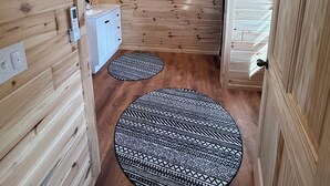 L’intérieur d’un chalet en bois comprend une salle de bain, un meuble blanc et deux tapis à motifs sur le sol.