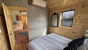 Une chambre dans un chalet en bois, comprenant un lit, une fenêtre avec des stores, un miroir et un appareil de climatisation.