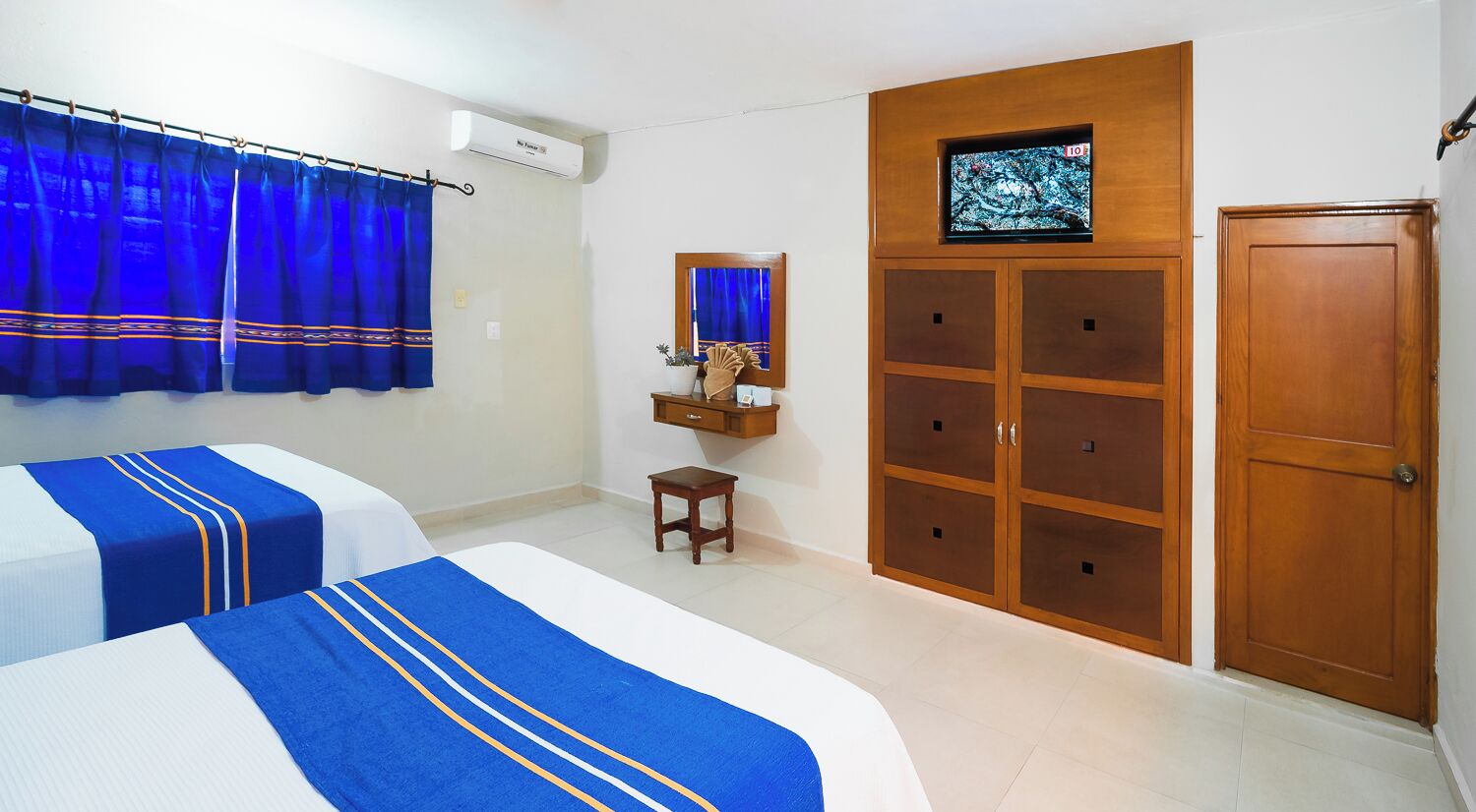A hotel room with two beds, a wooden wardrobe, a small table, and a TV on the wall.