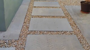 Un vialetto conduce all'ingresso di un edificio con una porta nera, circondato da ciottoli e piante in vaso.