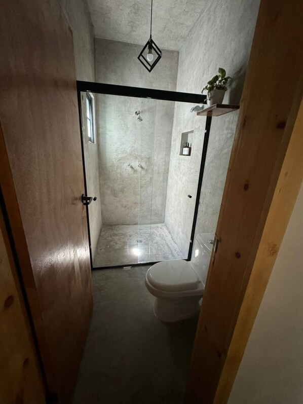 Un baño pequeño y estrecho con ducha, inodoro y una lámpara colgante.