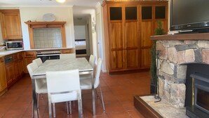 Une cuisine avec des meubles en bois, une cheminée en pierre, une table à manger avec des chaises et un téléviseur posé sur un meuble.
