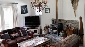 A cozy living room with a leather sofa, a television, a stone fireplace, and a decorative chandelier. - Jagungal 2 - Thredbo (Thredbo)