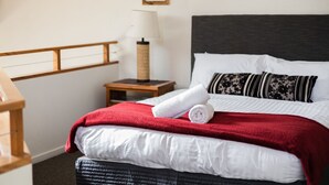 A neatly made bed with white and red bedding, a dark headboard, and a small bedside table with a lamp. - Jagungal 2 - Thredbo (Thredbo)