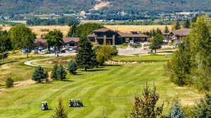 A golf course with a clubhouse, a parking lot, and a mountainous backdrop.