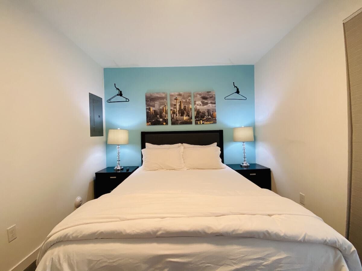 Een net opgemaakt bed in een hotelkamer, met een stadsgezicht op de muur, twee bedlampen en een nachtkastje.