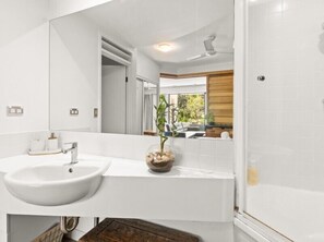 Un baño moderno con un lavamanos blanco, un espejo y una zona de ducha.