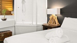 A modern hotel room with a glass-enclosed shower, a wooden headboard, a bedside table with a plant, and neatly folded towels. - Casuarina Apartment 200m from the Beach (Casuarina)