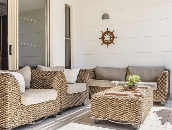 Un espacio exterior moderno con mobiliario de mimbre y un reloj decorativo en la pared.