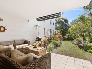 Un patio con mobiliario de mimbre, una parrilla y plantas en macetas.