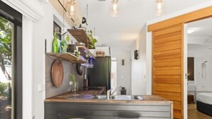 A compact kitchen with a wooden countertop, two stools, and hanging plants. - Casuarina Apartment 200m from the Beach (Casuarina)