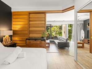 Habitación de hotel moderna con una cama grande, paneles de madera, un sofá y vistas a zonas verdes a través de amplios ventanales.