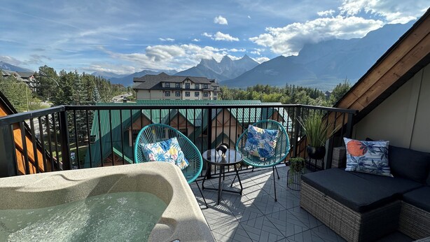 A balcony with a hot tub, wicker furniture, and a view of mountains.