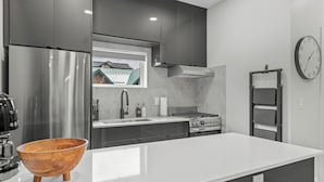 A modern kitchen with a stainless steel refrigerator, a wooden bowl on the counter, a stove, and a clock on the wall.