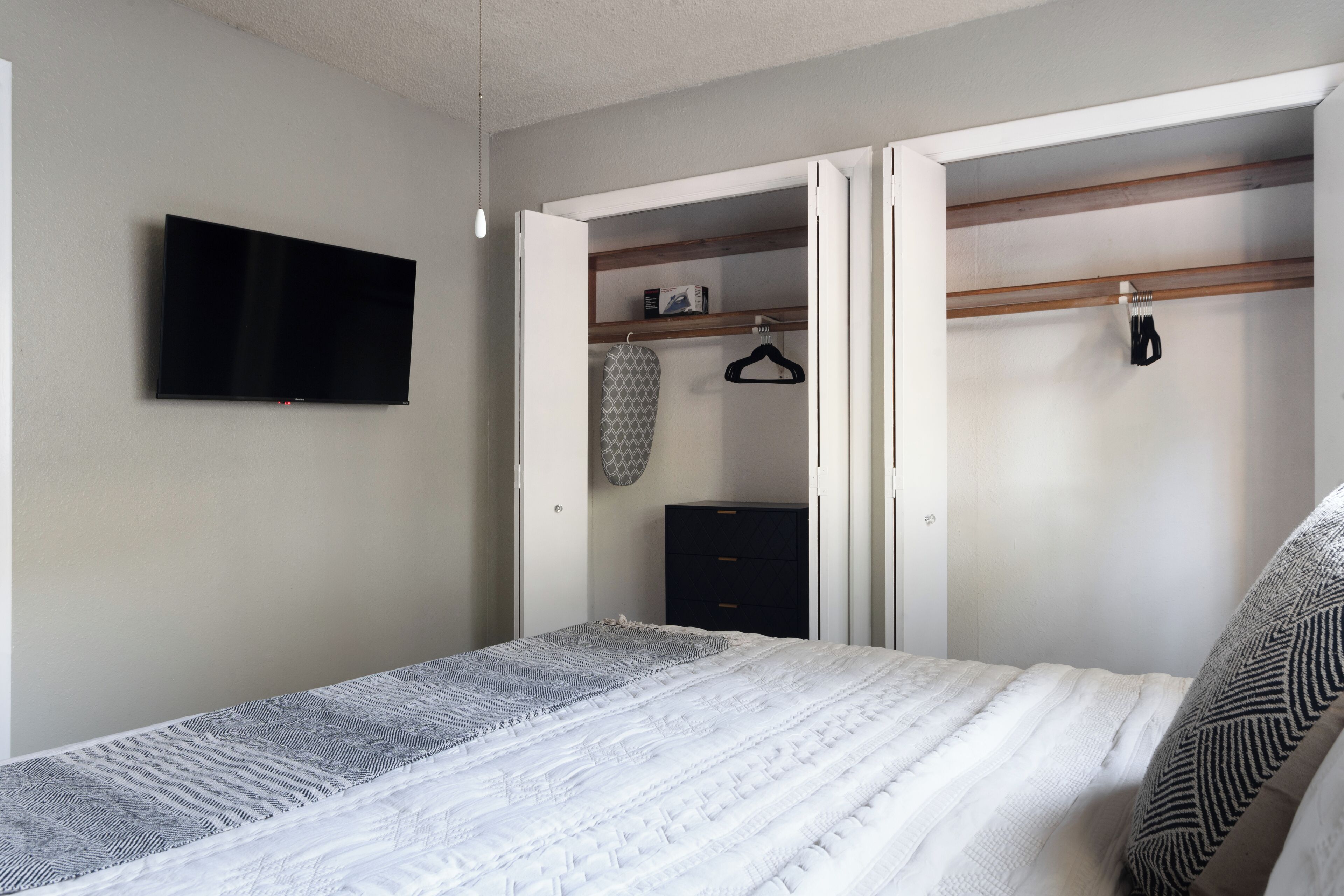 Une chambre à coucher comprenant un lit, un téléviseur fixé au mur, une armoire avec une tringle pour suspendre les vêtements et une petite commode.