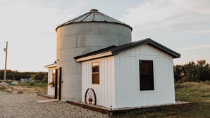 Ein kleines weißes Gebäude mit einem angebauten Silo, einem hölzernen Wasserrad und einer Schotterauffahrt.