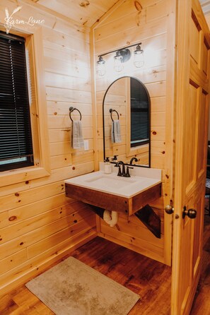 A wooden cabin bathroom with a sink, mirror, and window. - Quaint handicap accessible cabin- Perfect for a cozy getaway (Bancroft)