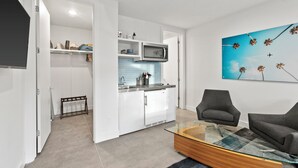 Une cuisine moderne avec des meubles blancs, un four à micro-ondes et un pare-feu en carreaux bleus. On y trouve également un coin repas avec une table en verre et deux fauteuils gris.